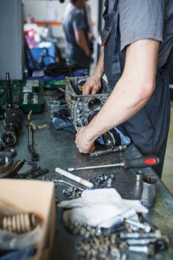 Servis istasyonunda araba tamiri. Direksiyonsuz asansörde arabayı tamir eden, lastiği tutan ve mekanik işleri tutan tulumda bir tamircinin elleri.