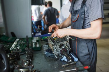 Servis istasyonunda araba tamiri. Direksiyonsuz asansörde arabayı tamir eden, lastiği tutan ve mekanik işleri tutan tulumda bir tamircinin elleri.