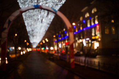 Akşamları desenli şehir sokaklarında Noel ışıkları altında çelenkler bulanık. Bokeh tatil ışıklarında şehrin arka planı