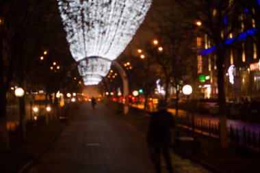 Akşamları desenli şehir sokaklarında Noel ışıkları altında çelenkler bulanık. Bokeh tatil ışıklarında şehrin arka planı