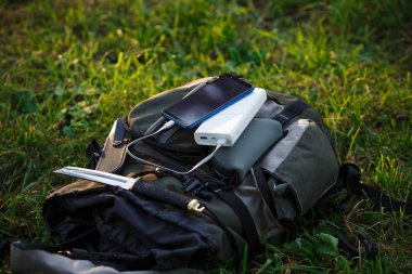 Sahada telefonunuzu ve aletlerinizi şarj etmek için bir güç bankasını kullanıyorsunuz. Sırt çantasında, kütükte, turist minderinde beyaz taşınabilir pil şarjı..