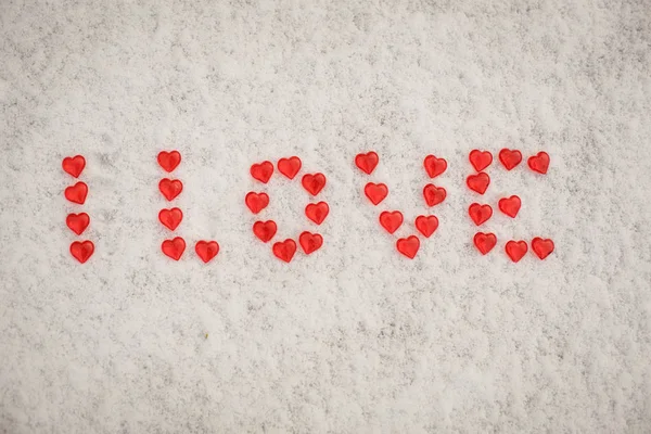 The word Love is made of red glass hearts on white snow. Symbols for Valentine\'s day, background with snow texture and hearts