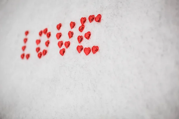 The word Love is made of red glass hearts on white snow. Symbols for Valentine\'s day, background with snow texture and hearts