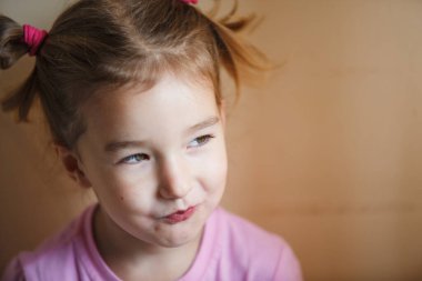 3 yaşındaki kurnaz küçük bir kızın duyguları. Kafasında iki parlak kuyruğu olan yakın plan bir kız sinsice gülümsüyor.