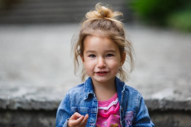 3 yaşındaki kurnaz küçük bir kızın duyguları. Saçları dağınık, kot ceket giymiş ve tahrik edici bir şekilde gülümseyen yakın plan bir kız.