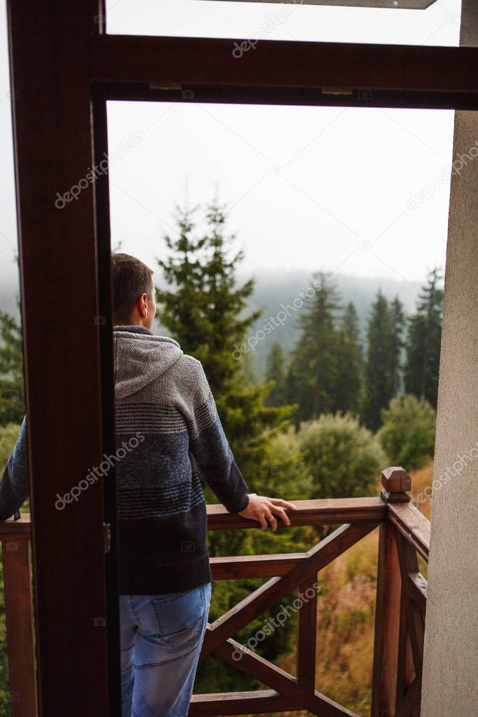 A young man in the morning looks from the hotel balcony with a view of the mountains, the fog and the fir forest. Mountain views at the Pamporovo hotel in Bulgaria in a ski resort