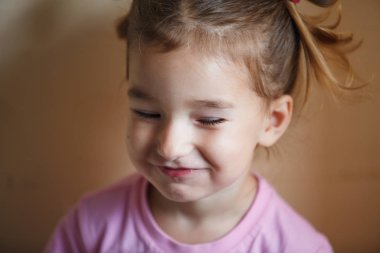 3 yaşındaki kurnaz küçük bir kızın duyguları. Kafasında iki parlak kuyruğu olan yakın plan bir kız sinsice gülümsüyor.