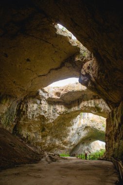 Tepesinde yuvarlak delikler olan büyük taş bir mağaranın yüksek kemerleri, mağaranın içinde çitleri olan turistik bir yol. Bulgaristan 'ın doğal cazibe-Devetashka mağarası