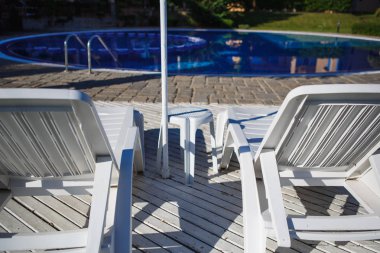 Havuzun yanında beyaz plastik güneş yatakları. Havuzun yanındaki otel dinlenme tesisi.