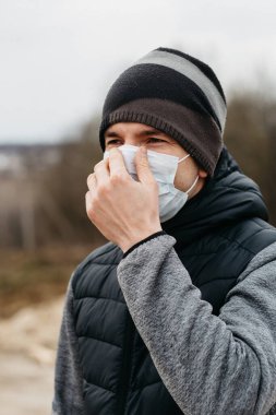 Korunaklı tıbbi maskeli bir adam. Karantina koşullarında koronovirüse karşı modern önlemler. Sıradan tarzda genç bir adam boş bir yolda yürüyor.