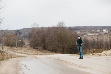 Korunaklı tıbbi maskeli bir adam. Karantina koşullarında koronovirüse karşı modern önlemler. Sıradan tarzda genç bir adam boş bir yolda yürüyor.