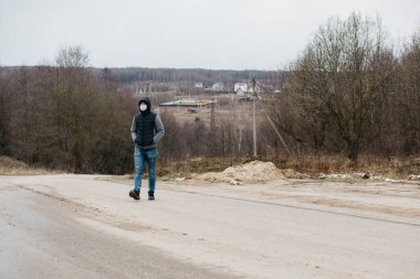 Korunaklı tıbbi maskeli bir adam. Karantina koşullarında koronovirüse karşı modern önlemler. Sıradan tarzda genç bir adam boş bir yolda yürüyor.