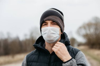 Korunaklı tıbbi maskeli bir adam. Karantina koşullarında koronovirüse karşı modern önlemler. Sıradan tarzda genç bir adam boş bir yolda yürüyor.