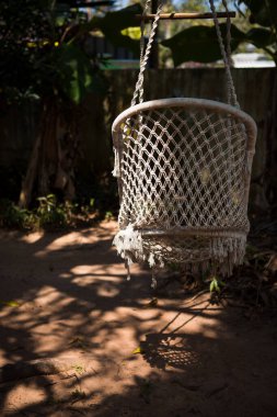 Bir hasır asılmış yaz sandalyesi tropik ağaçların gölgesinde asılı duruyor. Örgü örüyorum.