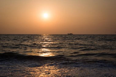 Hindistan 'da denizde turuncu gün batımı - turuncu ve pembe gökyüzü, koyu mavi deniz. Denizdeki ufuktaki bir geminin ana hatları.