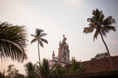 Hindistan 'daki Hristiyan Katolik Kilisesi, palmiye ağaçlarının tropikal yaprakları arasında Kerala. Hindistan 'da gün batımının pembe ışığında tapınağın beyaz duvarları.