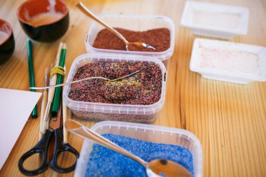 Evde, masada oturan çocuklar için yaratıcı eşyalar ve el sanatları. Boyalar ve fırçalar, makas, iplik ve kumaş kırıntıları - arka planda çocuğun ve ebeveynin elleri.