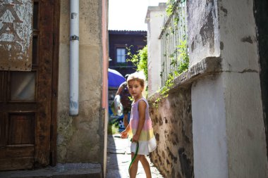 Sozopol, Bulgaristan-18 Eylül 2019. Evler arasında dar bir boşlukta küçük bir kız ve parlak bir güneş. Şehrin eski bölümünün dar sokakları