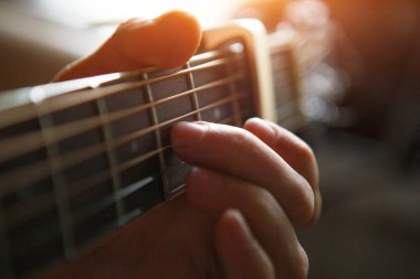 The fingers of a man's hand on the neck of a guitar clamp the strings close-up. Guitar playing, beautiful lighting, background with space for text clipart