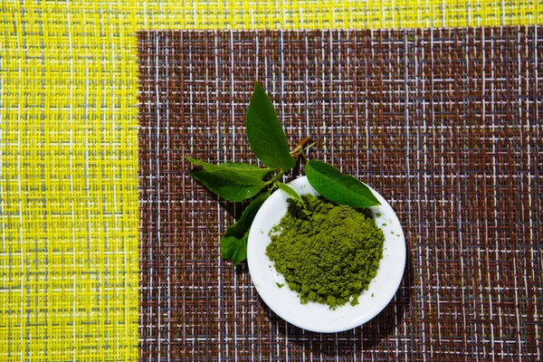 Japanese matcha green tea is poured into a white mug and on a white saucer in powder. Tea set on a textured napkin of natural flowers, decorated with a branch of green leaves. Background with space for text