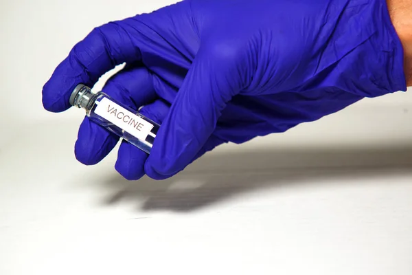 医生戴着蓝色医用橡胶手套的手拿着一个印有 Vaccine 字样的小瓶 医学概念 用药瓶来治疗这种流行病 白人背景 — 图库照片