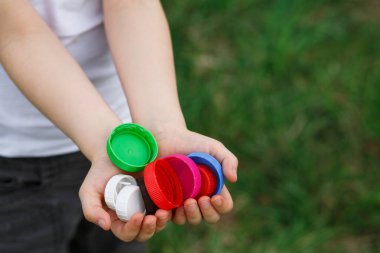 Küçük bir kız elinde plastik şişe kapağı tutuyor. Yetim çocuklara yardım etmek için gönüllü hayır etkinliği 