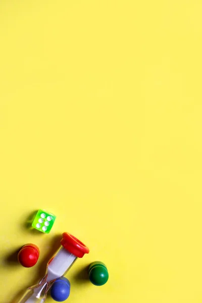 Game cubes, chips, hourglass on a yellow background. The concept of home Board games, classes at home with children, developmental training, logic games. Flatlay and space for text