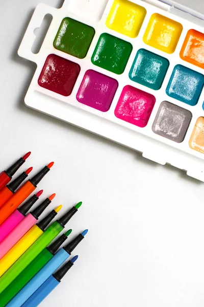 A palette of color watercolors with brushes and markers on a white background with space for text. Creative classes with children at home and at school, art master class, the concept of creative development. Desktop of the creative workshop-flatlay