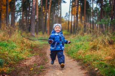 Küçük çocuk parkta yol boyunca sonbaharda çalışır. İki ayağını yerden ayrılır