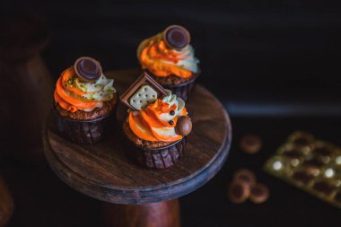 Turuncu-Beyaz krem çikolata, bisküvi ve tatlılar ile dekore edilmiş bir karanlık cam ile cupcakes karanlık bir arka plan üzerinde koyu renk ahşap bir stand üzerinde durmak