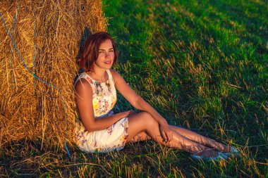 Bir yaz elbiseli bir kız çimlere bir haystack sırtına yaslanmış oturuyor. Bir kız alanında