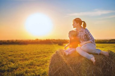 Anne ve oğlu günbatımında bir haystack ve sarılmak batan güneşin karşı bir alanını otur. Kırsal yaşam, bir yürüyüş ve doğa, şehir dışında bir tatil