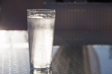 Su damlaları cam masaya yansıyan uzun buz gibi soğuk bir bardak su.