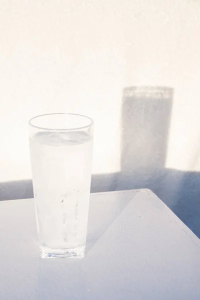 Tall Icy Cold Glass of Water with Water Drops  Casting a Shadow on White Wall