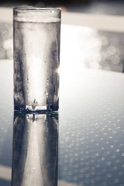 Tall Icy Cold Glass of Water with Water Drops Reflecting on Glass Table