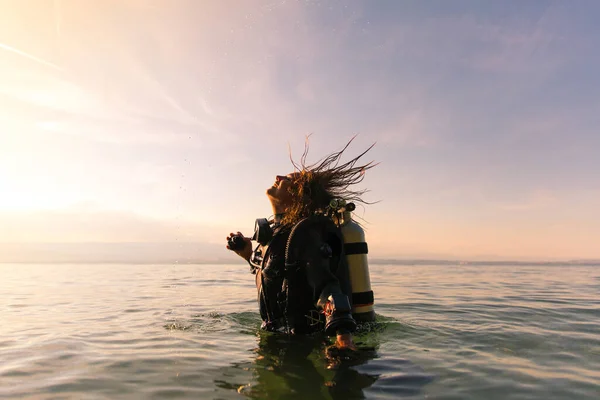 Female Scuba Dive Instructor Wearing a Dry Suit, a Twin Tank and Holding Fins Flipping Wet Hair in the Air