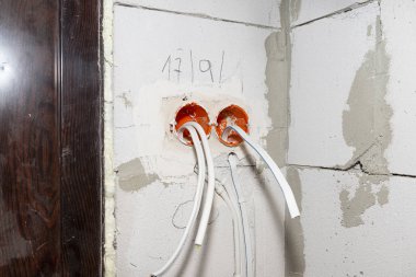 Turuncu, yuvarlak bağlantı kutusu beyaz duvara elektrik kablolarıyla monte edilmiş..