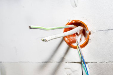 Turuncu, yuvarlak bağlantı kutusu beyaz duvara elektrik kablolarıyla monte edilmiş..