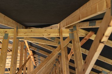 Çatı kirişleri yapım aşamasındaki müstakil bir evin zarı, içeriden görüş, görünür çatı unsurları ve kiriş plakaları ile kaplıdır..