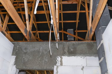 Yeni yapılmış çatı kirişlerine monte edilmiş bir evin plastik kablo borularındaki aydınlatma kabloları.