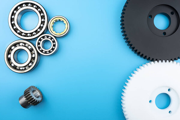 Ball bearing and black and white plastic gear lying on a blue background with copy space in the middle. Flat view from above.