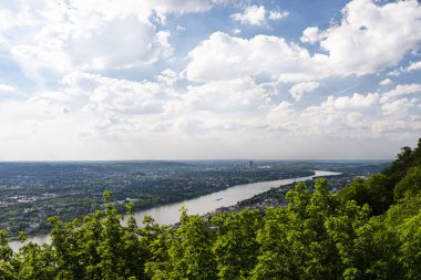 Batı Almanya 'da Rhein Nehri bulutlarla gökyüzüne karşı şehir boyunca akar. Nehirde görünür mavnalar ve gemiler.