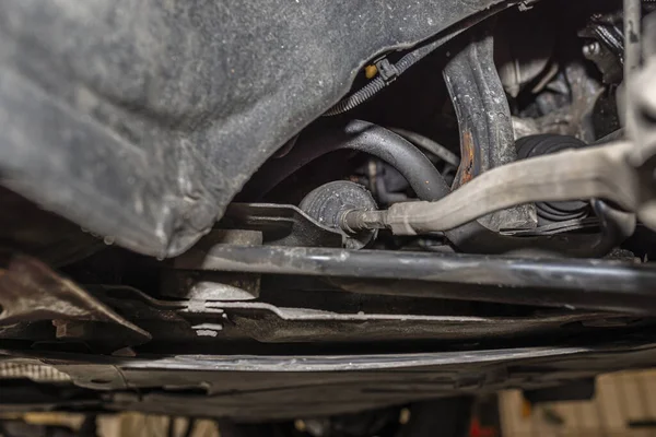 Steering stabilizer connected with steering knuckle, seen from the bottom of the car on a jack in the workshop.