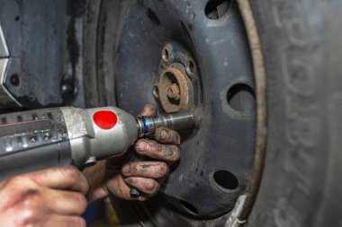 Araba tamircisi, araba atölyesinde pnömatik ingiliz anahtarıyla çelik araba tekerleğini sürgüler..