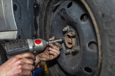 Araba tamircisi, araba atölyesinde pnömatik ingiliz anahtarıyla çelik araba tekerleğini sürgüler..