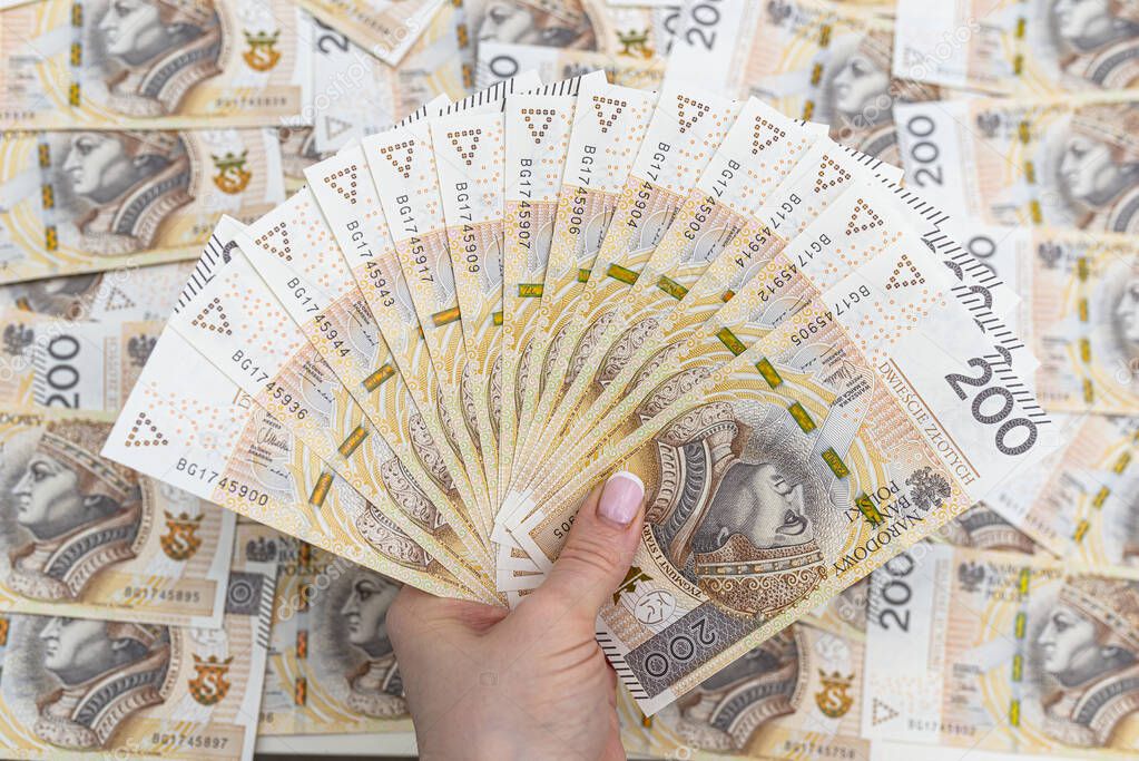 The woman is holding Polish banknotes on the front side, face value 200 PLN arranged in a fan, in the background a pile of Polish banknotes.