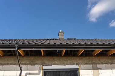 The roof of a single-family house covered with a new ceramic tile in anthracite against the blue sky, visible trusses. clipart