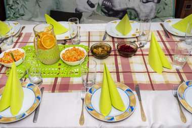 Yeşil peçeteler bir üçgen şeklinde tabaklar, sudan yapılmış limonata ve büyük bir sürahide portakal dilimleri, görünür salatalar..