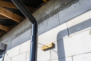 Binayı izole etmek için evin ham duvarına bağlanmış siyah metal bir oluk..