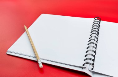 Beyaz sayfalı açık bir defter ve solunda ahşap bir kalem var. Kırmızı arka planda izole edilmiş..